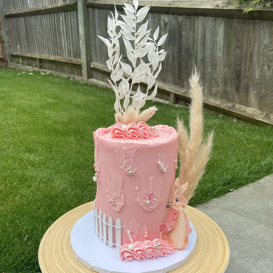 Baby Shower Cakes for Girls a Tall Pink Cake with Flowers and Plants Coming From It Outside on a Table