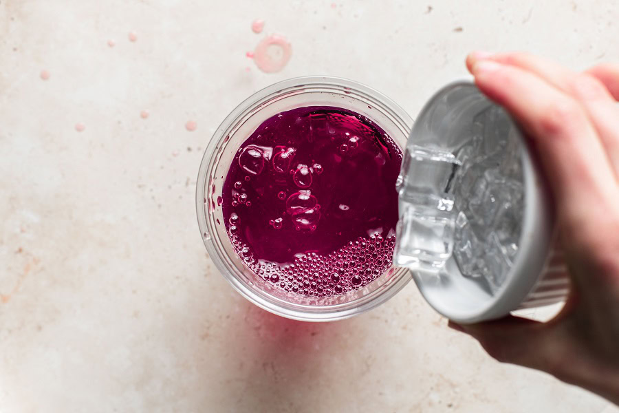 Copy Cat Starbucks Mango Dragon Fruit Refresher Recipe Overhead View of a Cup with a Person Holding a Shaker of Ice Above the Cup