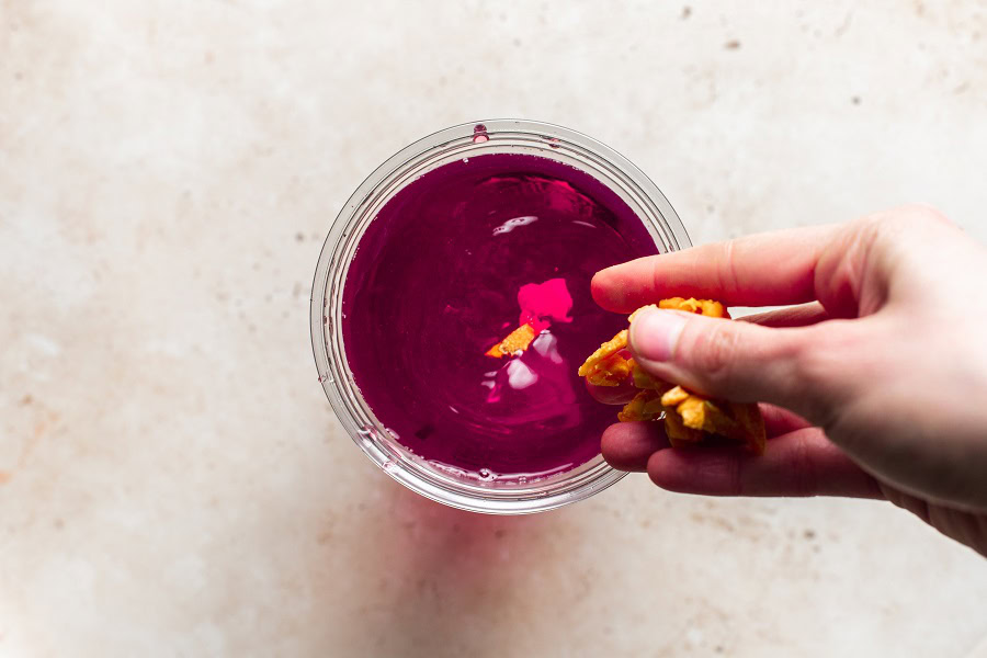 Starbucks Mango Dragon Fruit Refresher Recipe Overhead View of a Cup of Refresher with a Person Putting Mango Bits into the Cup