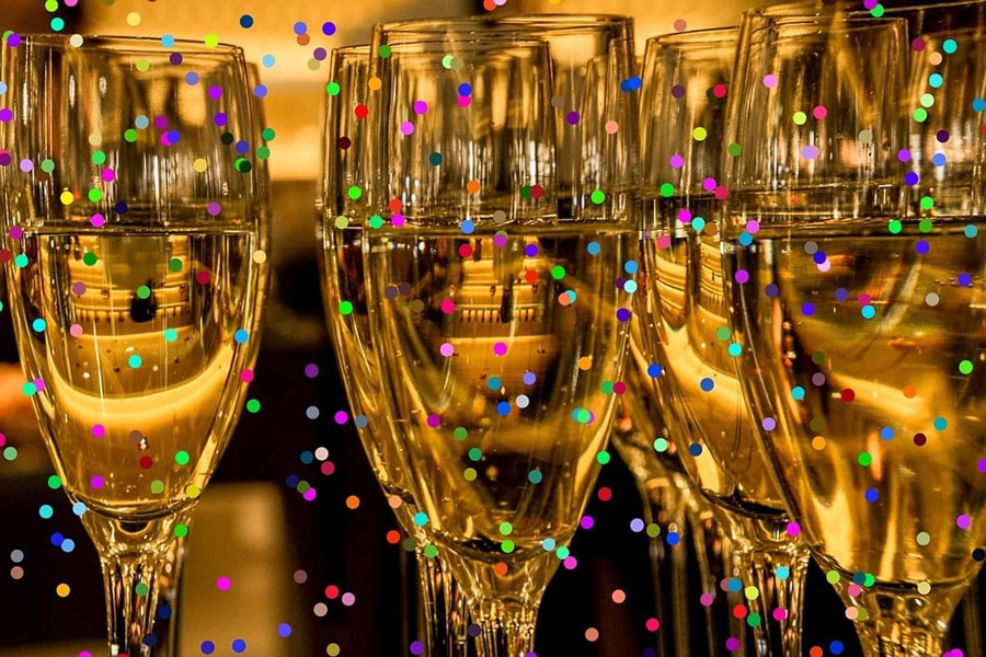 Pitcher Cocktails Close Up of Champagne Flutes Filled with Champagne and Colorful Confetti Falling Around Them