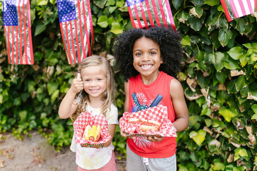 4th of July Cookies Two Young Girls Holding Plates of BBQ Food Outside in Front of a Bush with American Flag Decorations