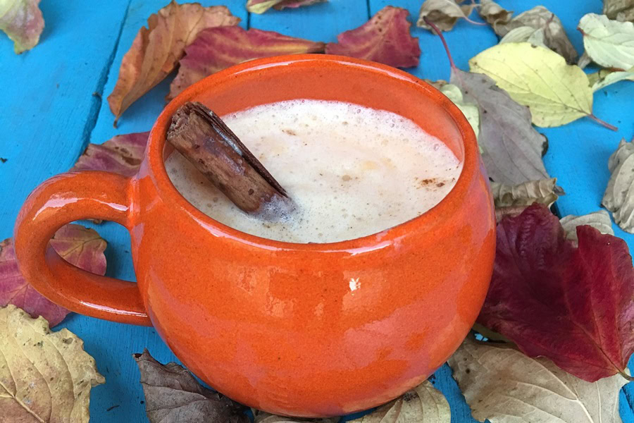 Funny Pumpkin Spice Memes to Go With That Latte Close Up of an Orange Coffee Mug Filled with Pumpkin Spice Latte on a Blue Wooden Table with Fall Leaves All Around