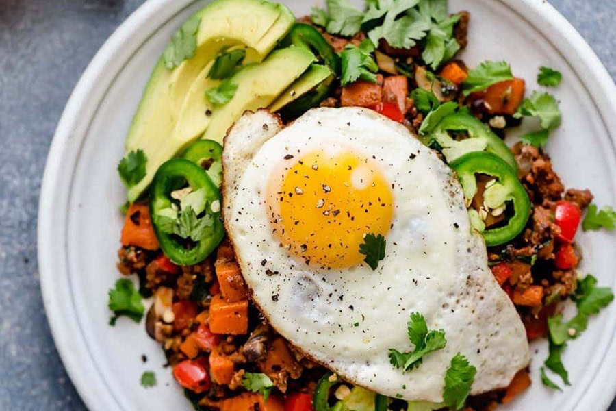 Whole30 Breakfast Recipes a Plate of Sweet Potato Hash Topped with an Over Easy Egg and Avocado Slices