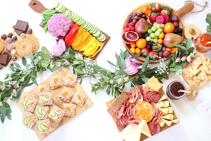 Mother&rsquo;s Day Brunch Decor Ideas Assorted Charcuterie Boards with Sliced Meats, Breads, Cheeses, and Fruit with Flowers Weaving Between the Trays