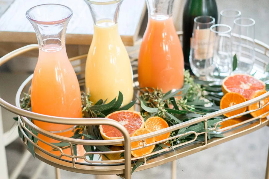 Mother&rsquo;s Day Brunch Decor Ideas Three Pitchers of Mimosa's Next to a Bottle of Champagne on a Serving Cart