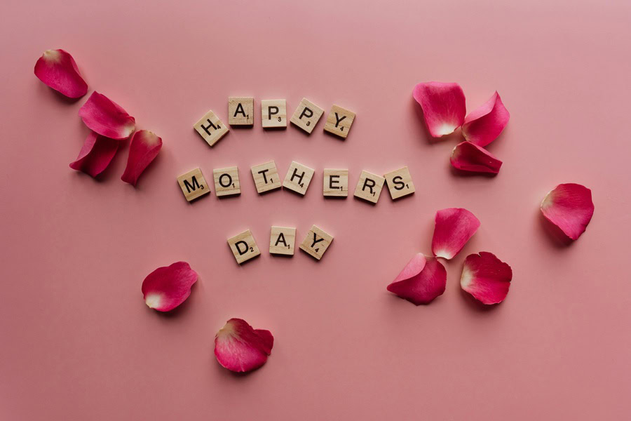 Mothers Day Quotes Letter Tiles Spelling Out Happy Mothers Day with Rose Pedals Sprinkled Around Them