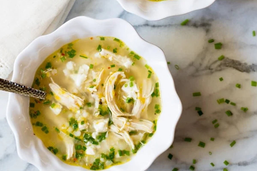 Greek Lemon Chicken Soup a White Bowl Filled with Greek Lemon Chicken Soup with a Spoon Sticking Out From The Soup