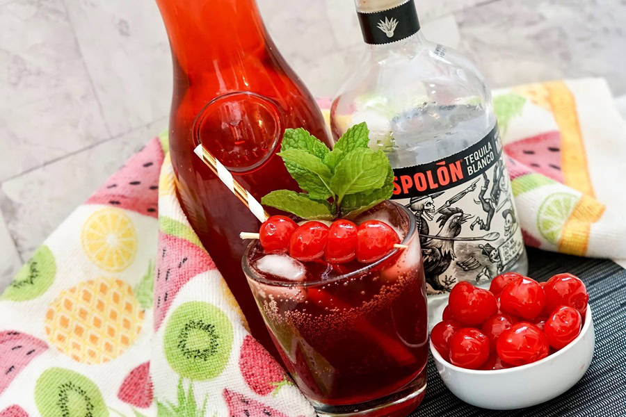 Tequila Drinks That Aren&rsquo;t Margaritas Tipsy Texan Cocktail in Front of Mixer and a Red Bottle A Small Bowl of Cherries Next to it
