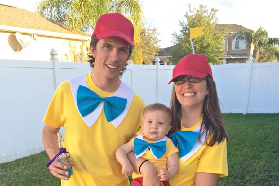 DIY Couple Halloween Costume Ideas a Couple Dressed as Tweedle Dee and Tweedle Dumb Standing in a Backyard Holding a Baby