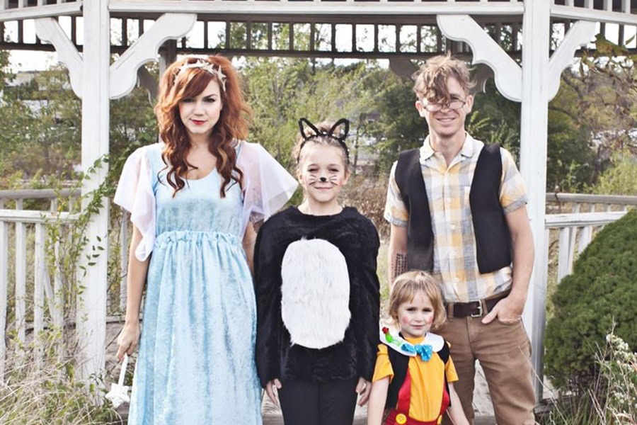 DIY Couple Halloween Costume Ideas a Man Dressed as Gepetto, a Woman as Blue Fairy a Girl as a Black Cat and a Little Boy as Pinocchio Standing Outside in a Park with a Gazebo in the Background